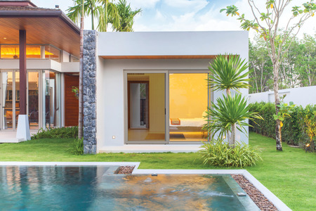 an exterior view of a sliding door with a screen on the left side facing a pool surrounded by a lawn and tropical plants